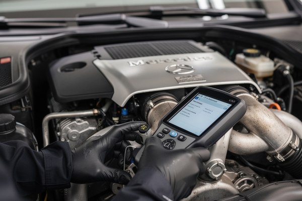 Mechanic inspecting a Mercedes-Benz engine bay with a diagnostic tool